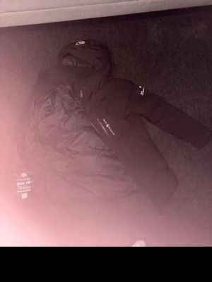 Svart dunjacka från sail racing - Säljer en svart dunjacka från sail racing med huva och diskreta loggor på bröstet och ärmen. Jackan har 500 fill power dunfyllning och är perfekt för kalla vinterdagar. Klassisk passform och dragkedja framtill. Snygg och funktionell för vintern.