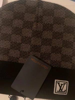  rutmönstrad mössa - Snygg mössa från  i svart och grått rutmönster. Mössan har en vikt kant med -logga framtill och är tillverkad i mjukt stickat material. Perfekt accessoar för att lyfta din outfit med en exklusiv touch.