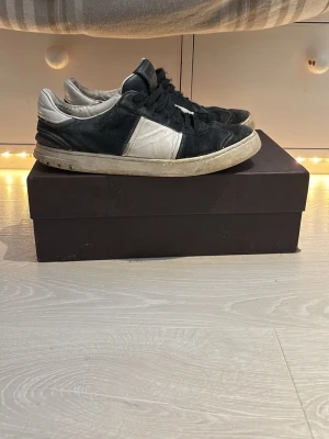 Svarta och vita sneakers från Valentino - Snygga sneakers från Valentino i svart mocka och vitt läder. Klassisk låg modell med svarta skosnören och vit sula. Diskret Valentino-logga på plösen. Perfekta för dig som gillar stilrena och exklusiva sneakers.