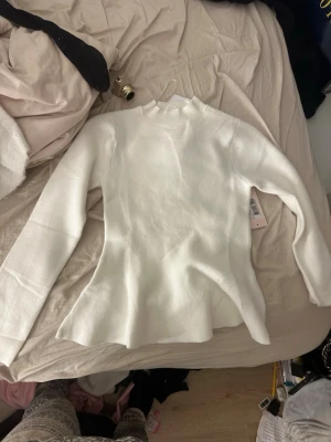 Vit ribbad långärmad topp - Säljer en vit stickad topp med lång ärm och hög hals. Toppen har en figurnära passform och är tillverkad i ett mjukt material som ger en clean och stilren look. Perfekt att styla med jeans eller kostym för en enkel men snygg outfit.