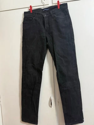 Svarta raka jeans från Levi's - Snygga svarta jeans från Levi's med rak passform och klassisk femficksdesign. Jeansen har bälteshällor, knappgylf och är tillverkade i ett slitstarkt denimtyg. Perfekta för en clean och stilren look.
