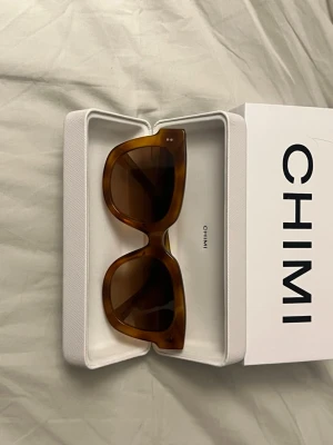 Bruna solglasögon från CHIMI - 08 HAVANA - Snygga solglasögon från CHIMI med bred, fyrkantig båge i brun ton. Glasen är mörka och bågarna har en glansig finish.  Kommer i originaletui. Inga repor eller fel