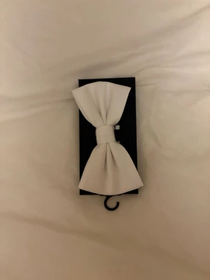 Vit fluga i klassisk modell - Snygg vit fluga i klassisk design, perfekt för att lyfta din outfit. Flugan är tillverkad i ett slätt tyg och har en stilren form med breda vingar. Passar till skjorta och kavaj för en elegant look.