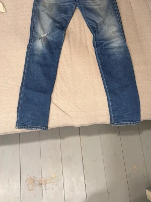 Blå raka jeans med slitningar - Säljer ett par klassiska blå jeans med raka ben och snygga slitningar på låret.