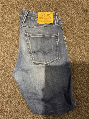 Replay anbass jeans - Snygga blå jeans från Replay med klassisk femficksmodell och ljusa slitningar framtill. Jeansen har raka ben och en gul patch med Replay-logga bak i midjan. Tillverkade i mjukt denimtyg som ger en skön känsla och cool look. W32 L30