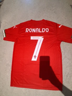 Ronaldo tröja puma - Röd Portugal fotbollströja från Puma med nummer 7 och Ronaldo på ryggen. Tröjan har vita detaljer, landslagets emblem på bröstet och gröna samt röda ränder på ärmarna. Med 1 puma på bröstet och två i armarna.                      Tveka inte att kontakta om du är intresserad eller har några frågor! Först till kvarn dom gäller!