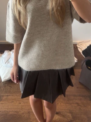 Mörkbrun plisserad kortkjol i skinnimitation - Snygg mörkbrun kortkjol med plisserad design i skinnimitation. Kjolen har en cool och edgy look som passar perfekt till en stickad tröja eller t-shirt. Enkel att styla för en trendig outfit.