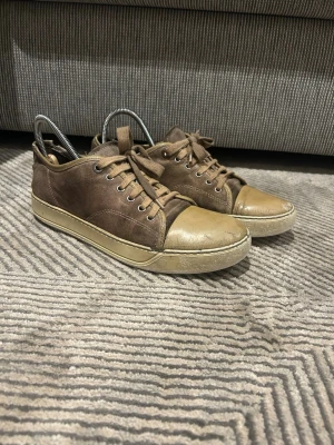 Beige lanvin skor i mocka och läder - Säljer ett par beige lanvin sneakers med lågt skaft, tillverkade i mocka och läder. Skorna har beige tåparti och sula, samt klassisk snörning med metallhål. Perfekta för en avslappnad och stilren look.