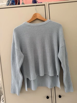 Ljusblå oversized stickad tröja - Säljer en ljusblå oversized stickad tröja med rund halsringning och långa ärmar. Tröjan har en avslappnad passform, ribbstickade muddar och en något längre bakdel för en cool look. Perfekt för lager på lager och chill stil.