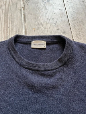 Merinoull tröja John Henric - Marinblå 100% merinoull tröja från John Henric med rund halsringning och ribbade muddar vid ärmslut och nederkant. Klassisk och enkel design i mjukt material, perfekt för lager på lager och stilrena outfits.