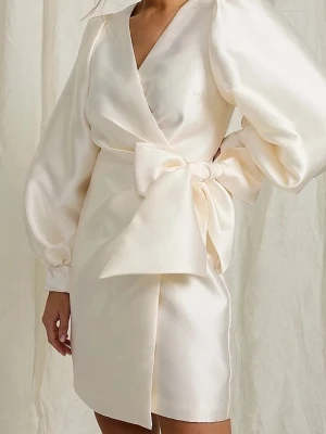 Vit omlottklänning med stor rosett - Elegant kort vit omlottklänning i satin med puffiga långärmar och bred manschett med klädda knappar. Perfekt för studenten! Nypris var 999kr! Pris kan diskuteras. 