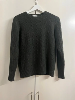Mörkgrön kabelstickad tröja Soft Goat - Mörkgrön kabelstickad tröja från Soft Goat i 100% kashmir. Tröjan har rund halsringning, långa ärmar och ribbade muddar vid ärmslut och nederkant. Perfekt för dig som gillar klassisk och stilren design. Skriv vid minsta fråga😊