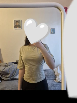 Ljusgrön croppad topp med knyt - Snygg ljusgrön croppad topp i bomull med halvlånga ärmar och rund halsringning. Toppen har en öppen rygg med breda band som knyts i en rosett bak, vilket ger en cool och trendig look. Perfekt att matcha med jeans eller kjol. Nästan helt ny, utan prislapp! Endast använd en gång