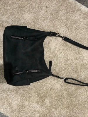 Svart axelväska med dragkedjor - Snygg svart axelväska i slätt konstläder med justerbar axelrem. Väskan har flera dragkedjefickor både fram och bak, samt stilrena detaljer i silver. Den har även flera innerfickor där inne❤️