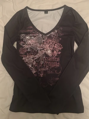 Svart långärmad topp med tryck från SHEIN - Snygg svart långärmad topp med v-ringning och detaljerat tryck i rosa och vitt framtill. Säljer eftersom att jag ångrade mig när tröjan kom fram så den är helt ny. Materialet är lite träningströja material typ❤️Men ändå bekvämt! V-ringningen går lite långt ner så ni vet, skriv till mig om ni vill ha bild på eller något annan bild på tröjan