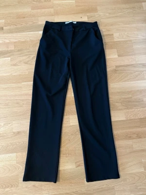 Svarta kostymbyxor från 157 - Snygga svarta kostymbyxor från 157 med raka ben och klassisk passform. Byxorna har hällor för skärp, knapp och dragkedja i gylfen samt diskreta fickor. Perfekta för en clean och stilren look.