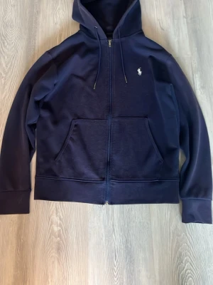 Ralph lauren zip hoodie  - Snygg mörkblå hoodie med dragkedja från Polo Ralph Lauren. Väl använd,Ett hål i mudden på ärmen och lite solblekt. Storlek S. Tveka inte på att höra av er!!