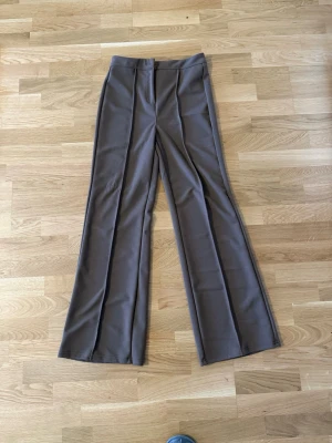 Bruna vida kostymbyxor från SHEIN - Snygga bruna kostymbyxor från SHEIN med hög midja och vida ben. Byxorna har pressveck framtill och är tillverkade i ett mjukt, stretchigt material som ger en skön passform. Perfekta för en trendig och stilren look.