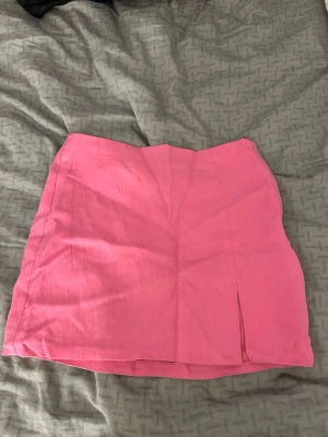 Rosa kortkjol med slits - Rosa kortkjol i enkel design med en liten slits framtill. Kjolen har en rak passform. Köpt från HM i storlek 34, använd endast ett fåtal gånger 