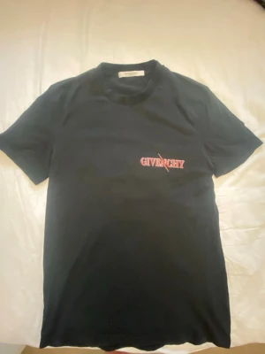 Svart Givenchy t-shirt med skorpion - Svart t-shirt från Givenchy med röd logga på bröstet och en stor, detaljerad skorpion med vingar på ryggen. Klassisk passform och rund halsringning. Perfekt för dig som vill sticka ut med en unik designertee.
