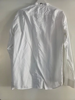 Vit skjorta från Selected Homme M - Klassisk vit skjorta från Selected Homme i regular fit. Skjortan är tillverkad i bomull och har långa ärmar samt knappar framtill. Perfekt basplagg för en clean och stilren look.