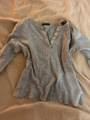 Ljusgrå ribbad långärmad topp - Säljer en ljusgrå ribbad långärmad topp från Abercrombie & Fitch. Toppen har v-ringning med knappar framtill och är tillverkad i mjuk bomullsmix. Perfekt för en avslappnad och stilren look.