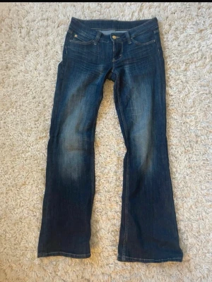 Mörkblå bootcut jeans från Nudie - Snygga mörkblå bootcut jeans från Nudie med klassisk femficksdesign och lätt slitning framtill. Jeansen har normal midja och är tillverkade i denim med stretch för extra komfort. Perfekta för dig som gillar en avslappnad men trendig look. Använt fåtal gånger. 