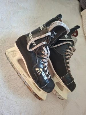 Svarta hockeyskridskor Dodist - Typ rostiga...Svarta hockeyskridskor från Dodist med vita snören och vita detaljer. Skridskorna har robust konstruktion, högt skaft och klassisk design. Perfekta för isträning eller spontanspel på isbanan. Metallblad och slitstark ovandel.