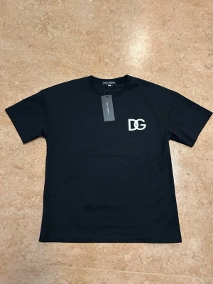 Svart DG t-shirt från Dolce & Gabbana - Svart t-shirt från Dolce & Gabbana med DG-logga i vitt på bröstet. Klassisk rund halsringning och korta ärmar. Tillverkad i mjuk bomull