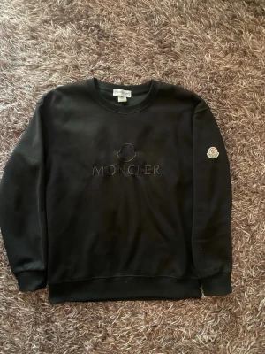 Svart sweatshirt från Moncler - Snygg svart sweatshirt från Moncler med broderad logga på bröstet och Moncler-märke på ärmen. Klassisk rund halsringning och ribbade muddar vid ärmslut och nederkant. Perfekt för en clean och stilren look.