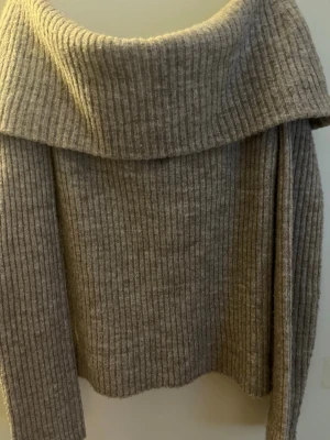 Beige ribbstickad tröja med stor krage - Mysig beige stickad tröja med bred, nedvikt krage och ribbstickat mönster. Perfekt för lager-på-lager och ger en avslappnad men ändå stilren look. Tröjan har långa ärmar och är tillverkad i ett mjukt material som känns skönt mot huden.