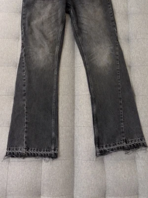 Säljer svarta flared jeans från zara  - Säljer ett par svarta flared jeans med slitna, råa kanter nertill. Jeansen har en tvättad look med ljusare partier på låren och är tillverkade i denim. Perfekta för en avslappnad och trendig stil.