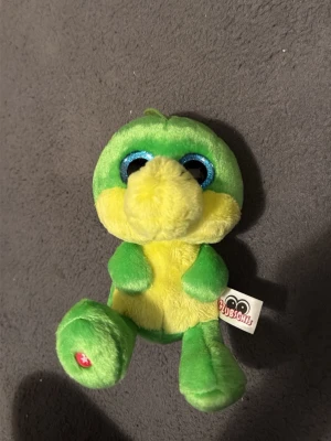 Grön och gul Club Petz mjukisdjur - Söt mjukisdjur från Club Petz i grönt och gult plyschmaterial. Den har stora blåglittriga ögon, mjuk nos och små taggar på huvudet. Perfekt som gosedjur eller dekoration. Märke finns på etiketten. Pris kan diskuteras 