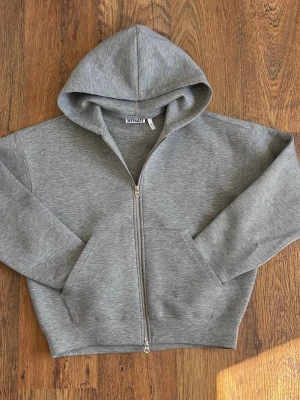 Weekday ”Simon Scuba” zip hoodie - Säljer en stilren grå simon scuba hoodie från Weekday med dragkedja framtill och stor huva. Hoodien har två rymliga fickor och är gjord i mjukt bomullsmaterial. Perfekt för en avslappnad look och enkel att matcha med allt.