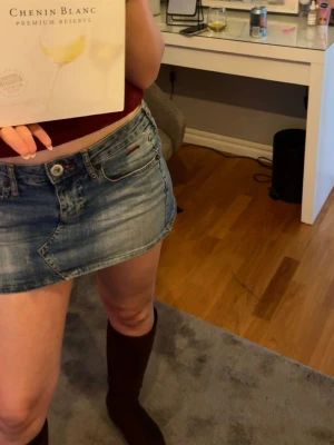 Blå jeanskjol i kort modell - Trendig kort jeanskjol i klassisk blå denim med femficksdesign och knappstängning framtill. Perfekt för dig som gillar en avslappnad och cool stil. Passar snyggt till både boots och sneakers.