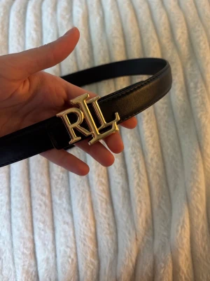 Svart skärp RLL - Stilrent svart skärp från Ralph Lauren med ett snyggt RL-spänne i guld. Finns även i brunt!🤍