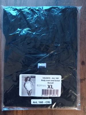 Svart body med smala axelband XL - Svart body från Valente med smala axelband, tillverkad i mjuk bomull. Perfekt för en stilren och bekväm look. Enkel design som passar till många outfits. Storlek XL 