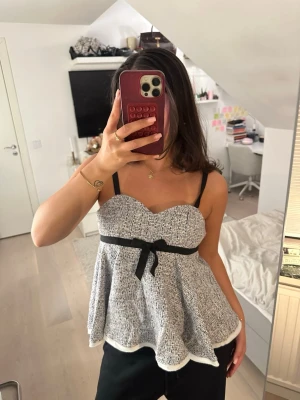 Blå blus med svart rosett och band (storlek S) - Supersöt blus från Zara i blått och vitt med svarta axelband och en svart rosett i midjan. Blusen har en hjärtformad urringning och är utställd nertill för en flowy look. Helt ny, aldrig använd men tagit bort prislappen.