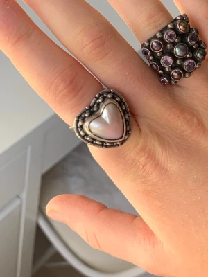Silverring med hjärta och pärlemor - Cool silverring med ett hjärtformat inslag av pärlemor i mitten och detaljerade små kulor runt om. Ringen har en vintagekänsla och passar perfekt för dig som gillar unika smycken med romantisk touch.