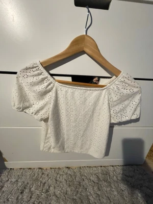 Vit broderad blus med puffärm - Supersöt vit blus med broderade detaljer och puffiga korta ärmar. Toppen har en fyrkantig urringning och är croppad, perfekt att ha till kjol och jeans. 