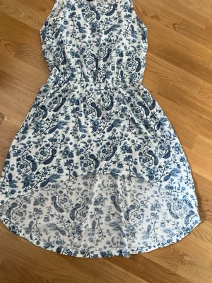 Vit och blå blommig sommarklänning - Säljer en vit klänning med blått blommigt mönster. Klänningen är ärmlös och har en lätt, luftig passform med markerad midja. Perfekt för varma dagar och har en rund halsringning. Materialet känns mjukt och bekvämt. Fungera även i storlek xs.