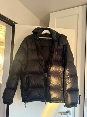 Svart pufferjacka från Ralph Lauren - Hej, säljer nu denna svarta Ralph lauren jackan som är i storlek M. Den är sparsamt använd och skicket är okej, 7/10 skick🔥. Perfekt för kallare kvällar, och mycket stilren. För mer frågor är det bara att DM:a ✅