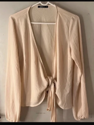 Beige omlottopp  - Snygg beige omlottopp från Gina Tricot med långa ärmar och knyt framtill. Tunt och luftigt material som passar perfekt till lager-på-lager. Enkel att styla med både jeans och kjol.