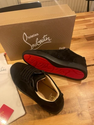Christian Louboutin svarta sneakers - Svarta sneakers från Christian Louboutin i mocka med ikonisk röd sula och svarta skosnören. Klassisk låg modell med diskret logga på insidan och lyxig känsla. Perfekta för dig som vill sticka ut med exklusiva detaljer och stilren design. HELT NYA OANVÄNDA. Storlek 42,43,44. Alla tillbehör Medföljer 