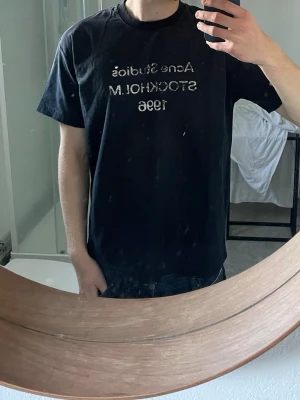 Svart Acne Studios t-shirt | M - Säljer en svart t-shirt från Acne Studios med trycket 'Acne Studios STOCKHOLM 1996' i vitt på bröstet. Klassisk rund hals och korta ärmar. Perfekt för dig som gillar stilrena och ikoniska plagg från populära märken.