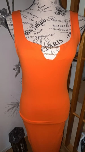 Orange ärmlös långklänning - Snygg orange långklänning med djup v-ringning och ärmlös design. Klänningen har en kroppsnära passform och är tillverkad i ett stretchigt material som ger en smickrande siluett. Perfekt för dig som vill sticka ut med färg och stil.