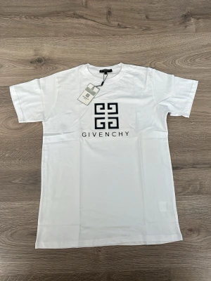 Vit Givenchy t-shirt med logga - Snygg vit t-shirt från Givenchy med stor svart logga och text på bröstet. Klassisk passform med korta ärmar och rund halsringning. Perfekt för en stilren och trendig look.