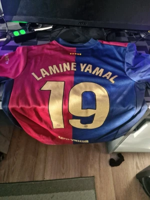 FC Barcelona matchtröja Lamine Yamal - Säljer en officiell FC Barcelona matchtröja med Lamine Yamal och nummer 19 på ryggen. Tröjan är i klassiska blå och röda färger, har klubbmärke och Spotify-logga på bröstet. Tillverkad i lätt och ventilerande material, perfekt för fotbollsträning.