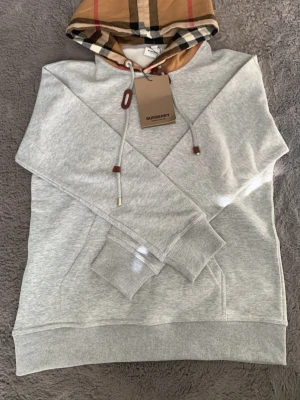 Bur*berry hoodie - En fin bur*berry hoodie i färgen grå med mönster på luvan. Vid frågor eller funderingar hör av dig. 