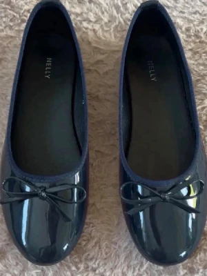 Svarta lackballerinaskor från Nelly - Stilrena marinblå ballerinaskor från Nelly i glansigt lackmaterial. Skorna har rund tå och en söt liten rosett framtill. Klassisk och enkel design som passar till många olika outfits. Perfekta för dig som gillar en clean och trendig look. Är använda en gång och därför inga defekter, tyvärr kommer de inte till användning och säljs därför!